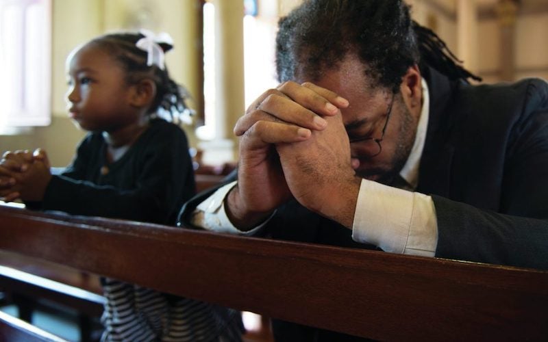 black father and daughter praying in pews