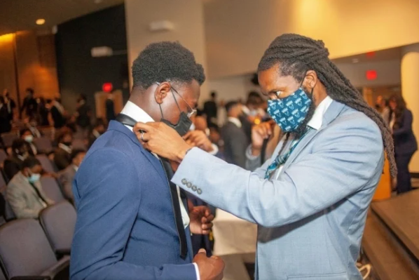 Calvin Hadley, assistant provost for academic partnerships and student engagement at Howard University, helps a business school student put on a tie as part of a ceremony for the You Lead Male Initiative, a support program for Black men business students.