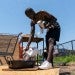 Man holding dog and pouring liquid into a large pan outside